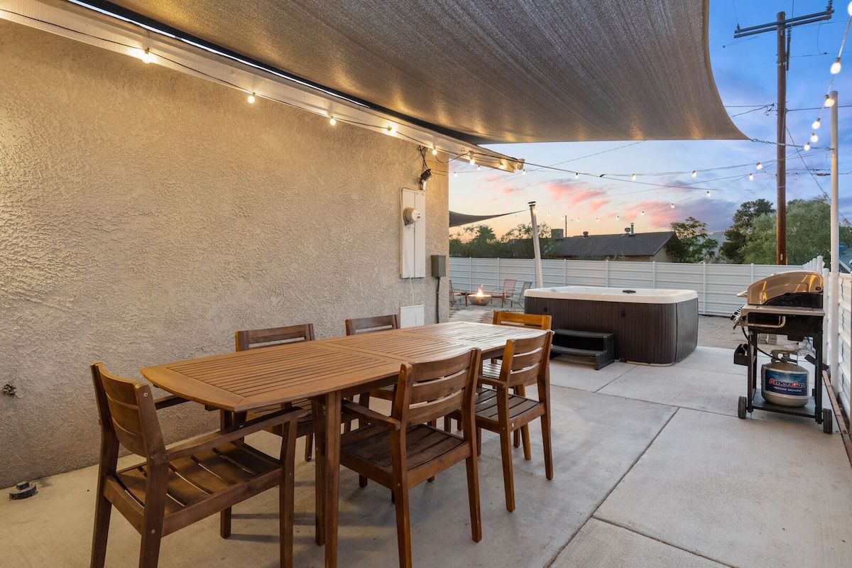 Une terrasse extérieure avec une table et des chaises en bois, un jacuzzi et un barbecue.