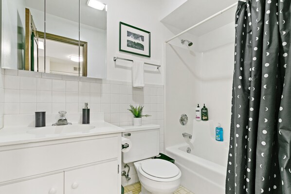 Une salle de bain avec un lavabo blanc, un miroir, des toilettes et une baignoire.