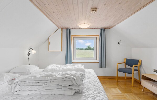 Un dormitorio con cama, una silla, un escritorio, una ventana con vista a un campo y una lámpara en el techo.