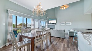 A spacious living area with a dining table, chairs, a chandelier, a television, and a view of the outdoors. - LARGE WATERFRONT HOUSE IN GULF SHORES, CLOSE TO EVERYTHING (Gulf Shores)