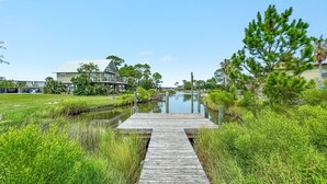 A wooden dock leading to a calm water body, surrounded by lush greenery and a house in the background. - LARGE WATERFRONT HOUSE IN GULF SHORES, CLOSE TO EVERYTHING (Gulf Shores)