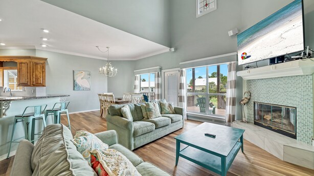 A spacious living area with a sofa, a coffee table, and a fireplace. There is a kitchen area with bar stools and a dining table. - LARGE WATERFRONT HOUSE IN GULF SHORES, CLOSE TO EVERYTHING (Gulf Shores)