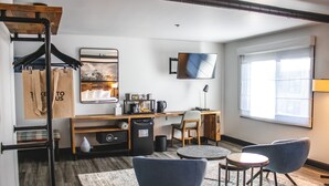 Ein modernes Hotelzimmer mit Schreibtisch aus Holz, einem Flachbildfernseher, einer Couch und zwei Sesseln.