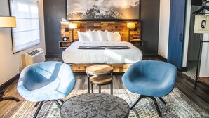 Ein Hotelzimmer mit einem Bett, zwei blauen Stühlen, einem kleinen Tisch, einem großen Gemälde an der Wand, einem Kleiderschrank und einer Lampe.