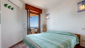 Ein Schlafzimmer mit Bett, Meerblick, Holztür und Stuhl am Fenster.