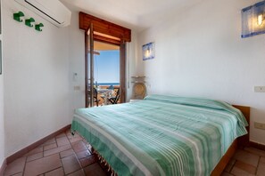 Une chambre à coucher avec un lit, une vue sur la mer, une porte en bois et une chaise près de la fenêtre.
