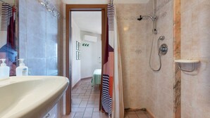 Ein Badezimmer mit einem großen Waschbecken, einer Dusche und einer Tür zu einem Raum mit einem Bett.