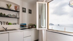 Eine Küche mit Meerblick, einem weißen Schrank, einer Spüle und einem Fenster mit Vorhang.