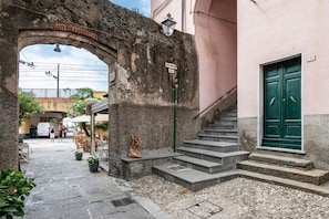 Un área de café al aire libre con escalones de piedra que conducen a la entrada de un edificio, una puerta verde y un arco de piedra.