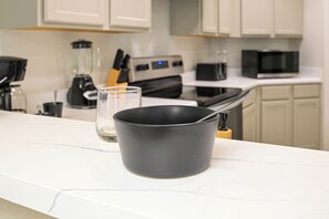 A kitchen with white cabinets, a black pot on the counter, and a glass.