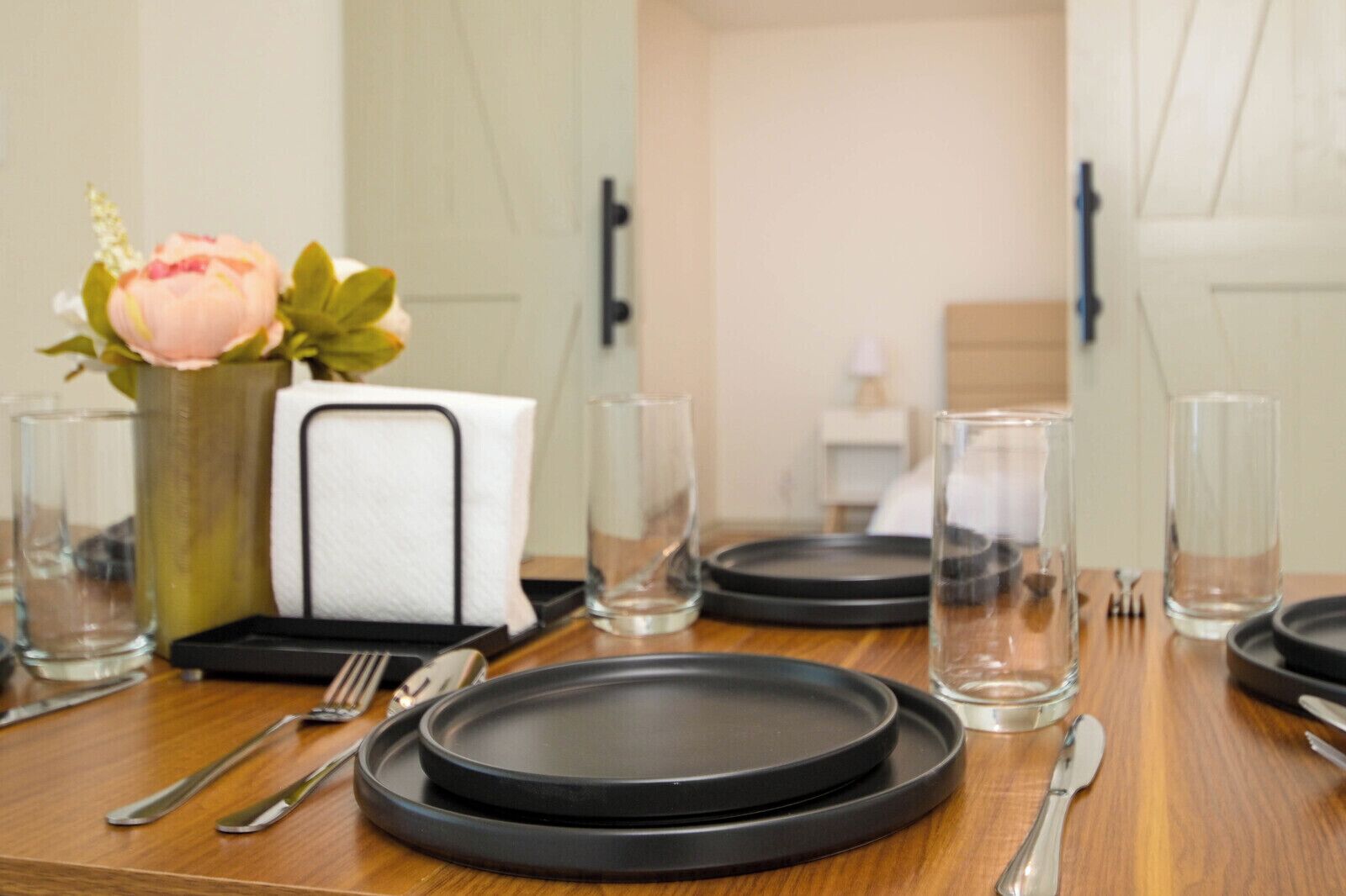 Quarto de hotel com uma mesa de jantar bem posta, um vaso com flores e uma cama ao fundo.