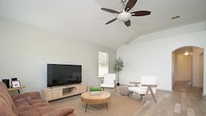 A modern living room with a flat-screen TV, a brown leather sofa, a wooden coffee table, and white chairs. - SeaWorld San Antonio! Quiet, 4-bedroom house. 12 guests. (San Antonio)