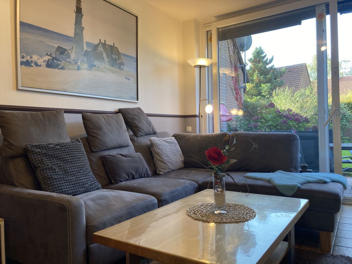 A living room with a brown leather sofa, a glass coffee table with a woven placemat, and a painting of a lighthouse.