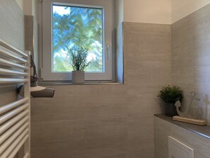 Een badkamer met een raam, een radiator, een potplant en een handdoekrek.