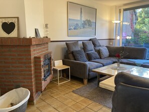 Una sala de estar acogedora con una chimenea de ladrillo, un sofá gris, una mesa de centro y un cuadro de un faro.