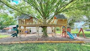 A playground with two wooden playhouses, slides, and a tree in the center. - enjoy ranch life.

 (Allen)
