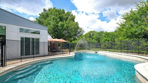 A swimming pool with a clear blue water, surrounded by a fence, and a building with large windows to the left. - enjoy ranch life.

 (Allen)
