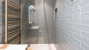 Un baño moderno con ducha, toallero dorado y pared de azulejos.