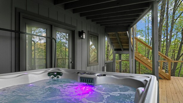Un bain à remous doté d’une terrasse en bois et de rampes, entouré d’arbres.