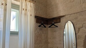 A bedroom with a bed, a wooden stool, a mirror, and a window with sheer curtains. - Charming suites among trulli in the heart of Alberobello (Alberobello)