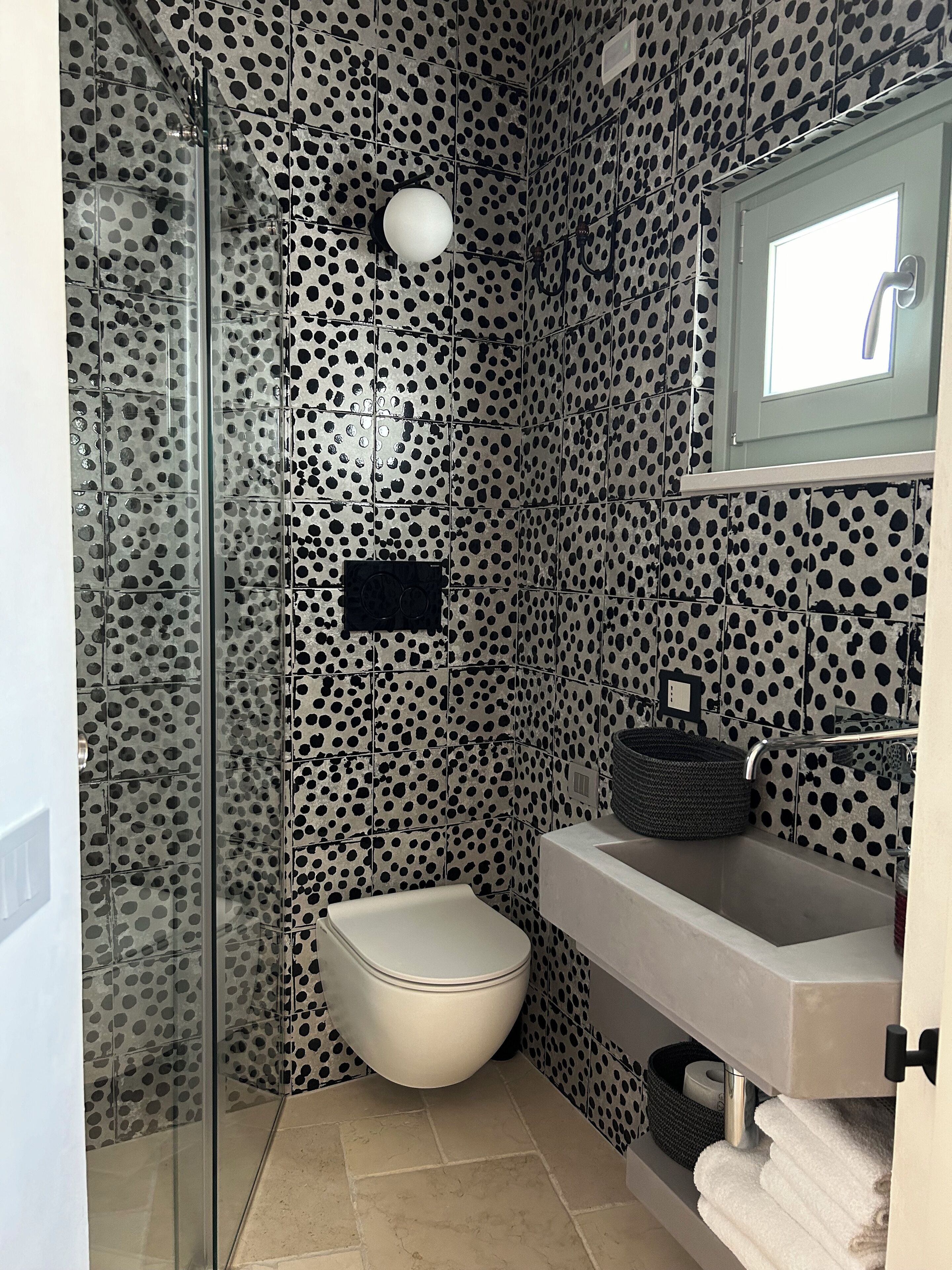 A bathroom with a polka dot tile design, a toilet, a sink, and a shower area.
