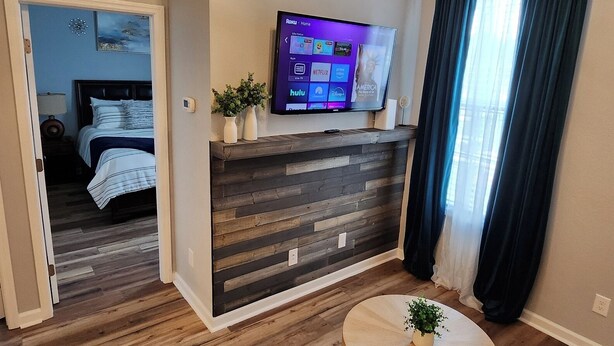 Een moderne woonkamer met een flatscreen televisie aan een houten wand, een ronde houten salontafel en een kleine potplant.