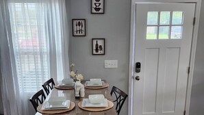Een eethoek met een houten tafel gedekt voor vier personen, witte stoelen en een witte deur met een raam.