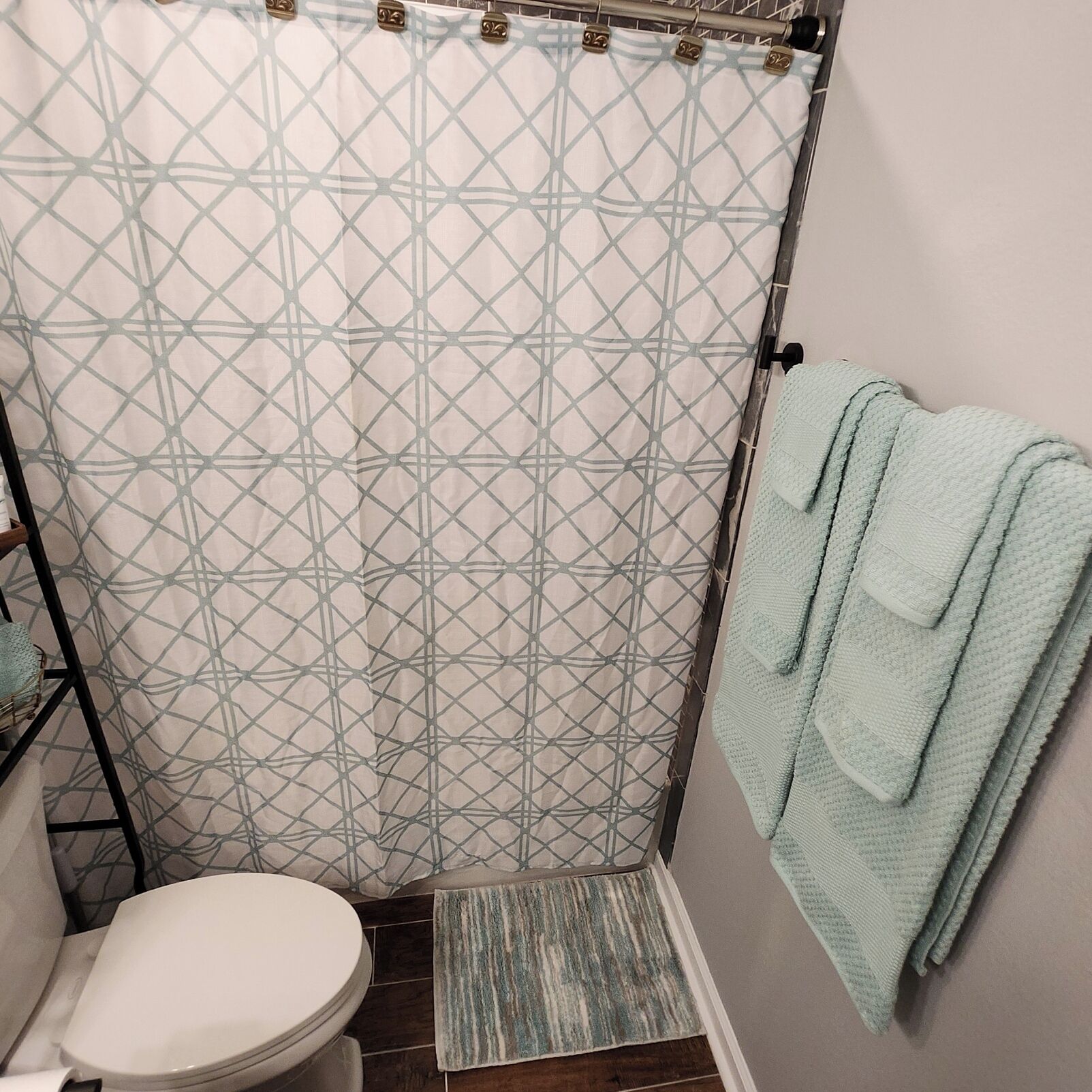 Un baño con cortina de ducha de estampado geométrico, un inodoro blanco, una toalla azul claro y una alfombra a rayas.