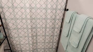 Un baño con cortina de ducha de estampado geométrico, un inodoro blanco, una toalla azul claro y una alfombra a rayas.