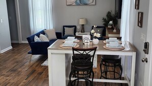 Een moderne woonkamer met een blauwe bank, een eettafel met stoelen en een plafondventilator.