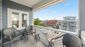 Ein Balkon mit Korbmöbeln, einem weißen Geländer und Blick auf angrenzende Häuser.