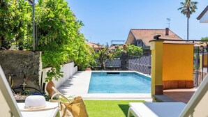 A swimming pool with a white deck, surrounded by a garden with green grass and trees. - Villa Cesare (Mascali)