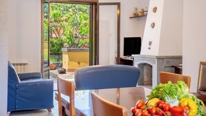 A modern living room with a dining area, a fireplace, and a view of a garden through a glass door. - Villa Cesare (Mascali)