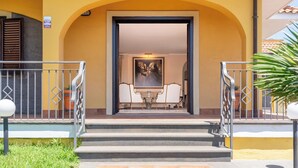 A hotel entrance with a staircase leading to a dining area with two tables and chairs. - Villa Cesare (Mascali)