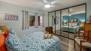 A bedroom with a bed, a chair, a desk, a mirror, and a window with curtains.
