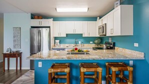 A kitchen with white cabinets, a stainless steel refrigerator, a microwave, and a granite countertop. There are three wooden stools at the island.