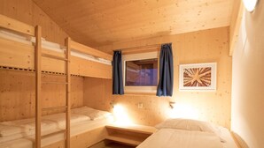 Een slaapkamer met een stapelbed, raam, ingelijste foto en bedlampje.