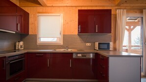 Een moderne keuken met rode kastjes, een inbouwoven, een magnetron en een raam boven de spoelbak.