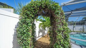 Un espace piscine agrémenté d’une clôture blanche et d’une arche recouverte de plantes grimpantes.
