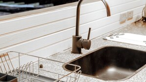 A kitchen with a stainless steel sink, a dish drying rack, and a wooden countertop.