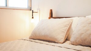 A bed with a quilted white cover, a wooden headboard, and a window with a view of a building.