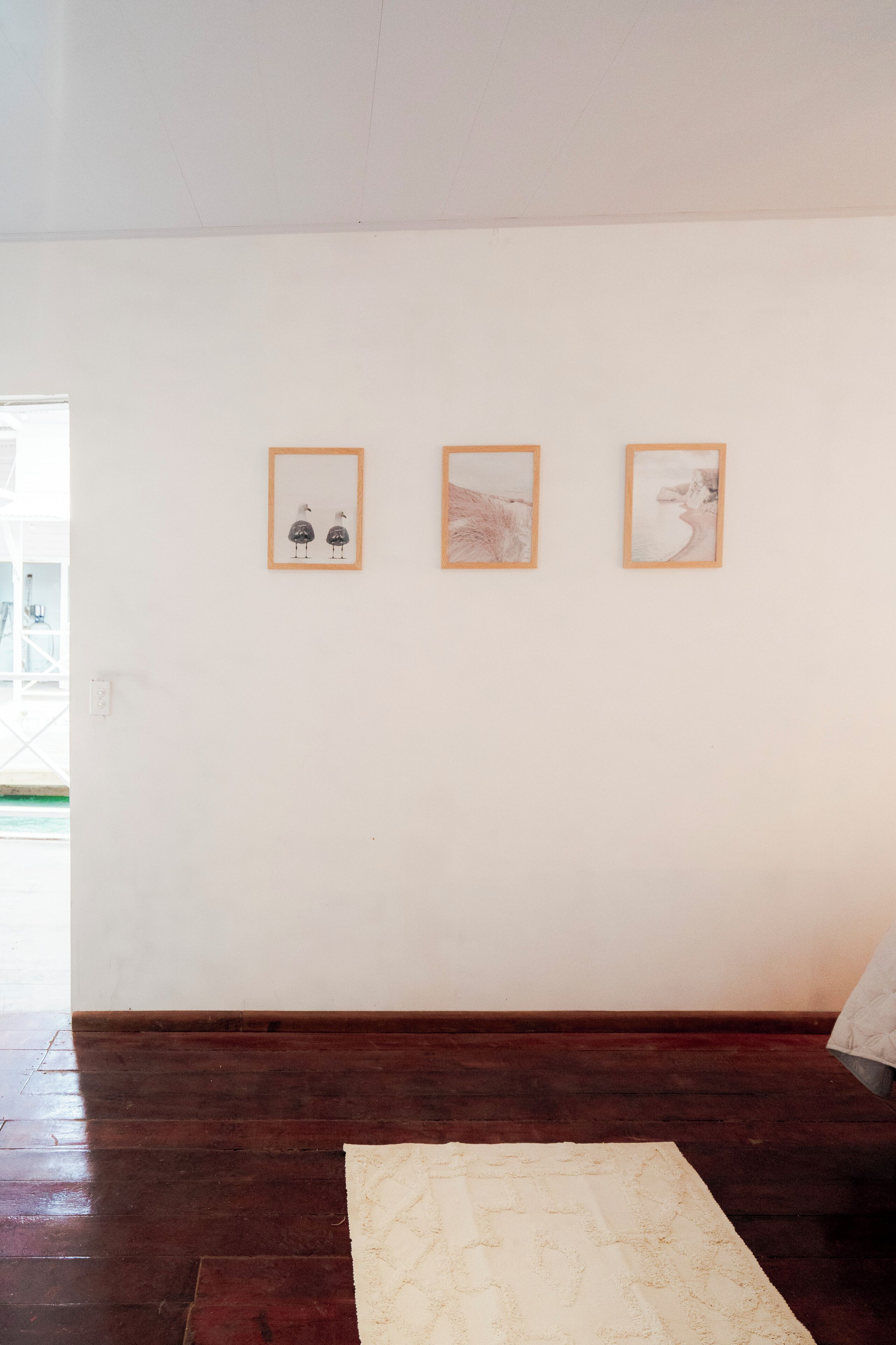 Ein Zimmer mit Holzboden, einer weißen Wand und drei gerahmten Kunstwerken.