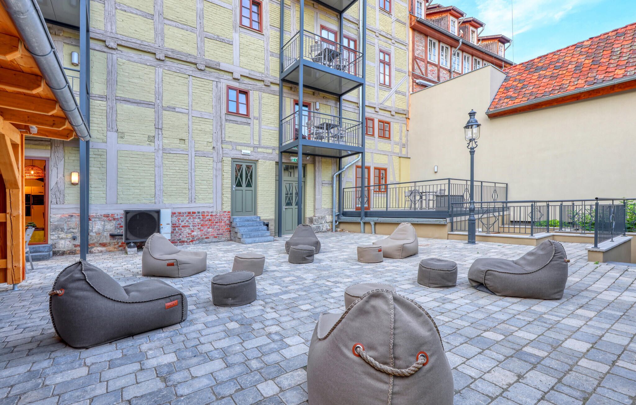 Un espace extérieur aménagé avec plusieurs fauteuils en forme de sac et un escalier menant à un bâtiment doté d’un balcon.