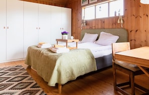 Une chambre à coucher avec un lit, une table de chevet, une lampe et une vue sur l’extérieur par une fenêtre.