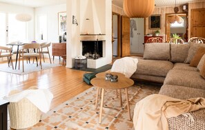 Un salon chaleureux avec une cheminée, un coin repas et une cuisine visible à travers une porte ouverte.