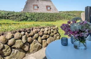 Una casa con techo de paja, pared de piedra y una mesa adornada con flores.