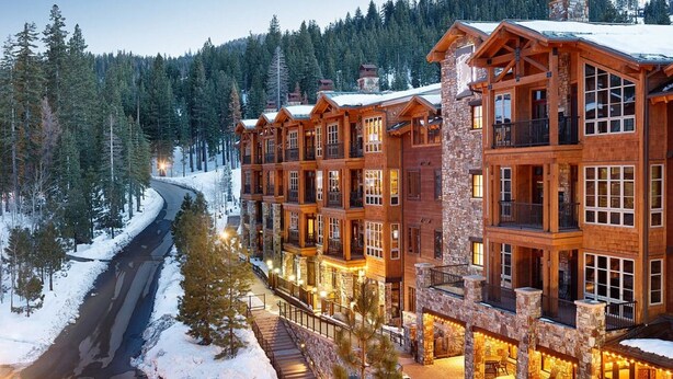 A multi-story lodge with a stone facade, large windows, and balconies, surrounded by a snowy forest.