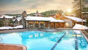 A resort with a swimming pool, stone buildings, and snow-covered roofs.