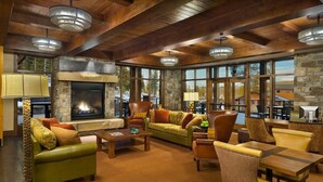 A cozy living room with a fireplace, comfortable seating, and large windows offering a view of the outdoors.