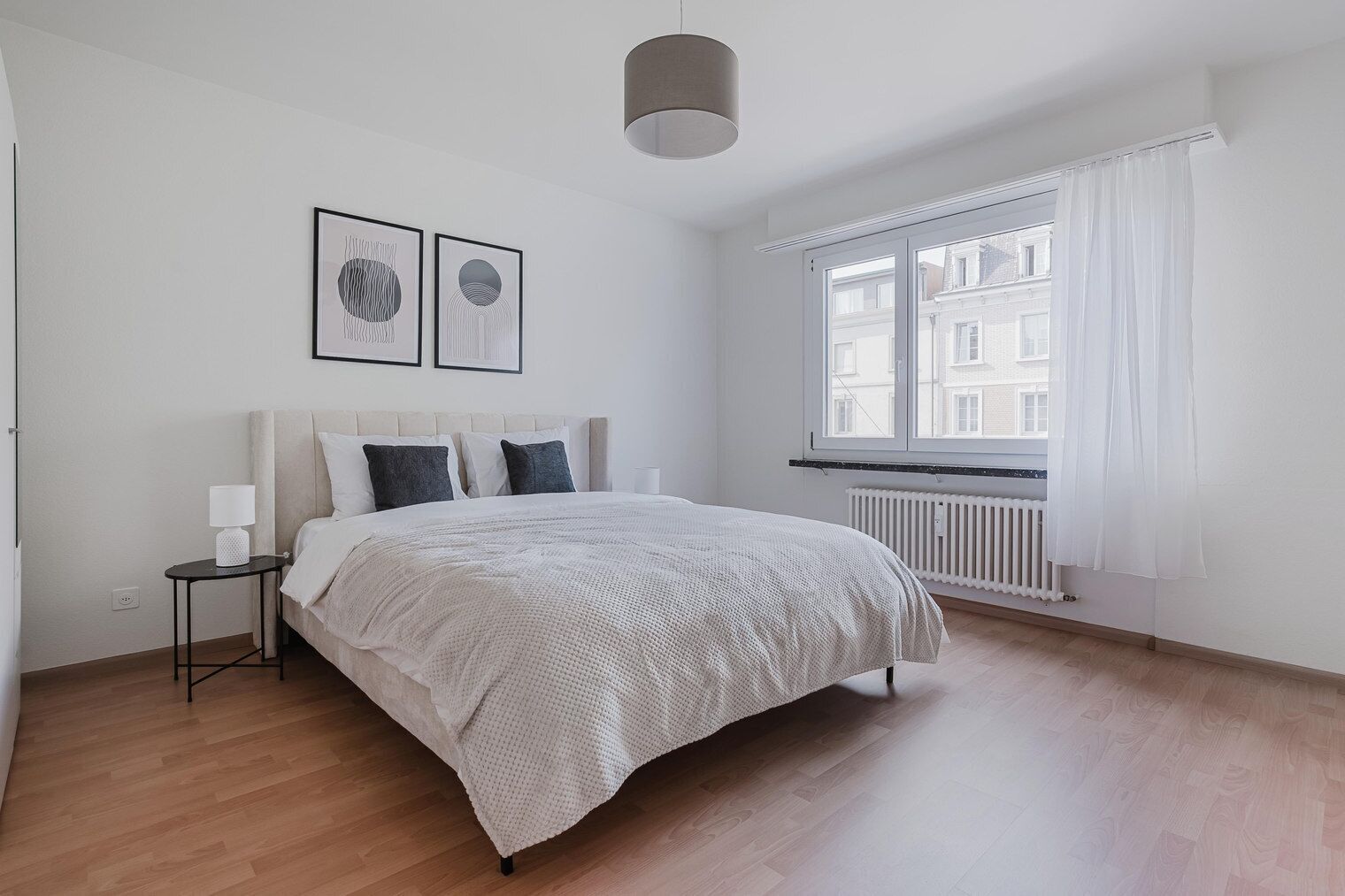 Un dormitorio con cama, mesita de noche, ventana con cortinas y radiador.